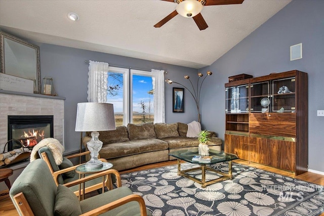 living room with a tile fireplace, ceiling fan, wood-type flooring, a textured ceiling, and vaulted ceiling