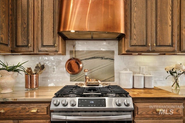 kitchen featuring wood counters, decorative backsplash, stainless steel gas range, and custom range hood