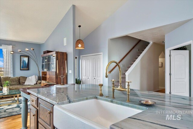 kitchen with sink, decorative light fixtures, high vaulted ceiling, light wood-type flooring, and light stone countertops