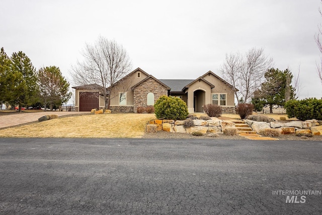 view of front of home with stucco siding, stone siding, a garage, and driveway