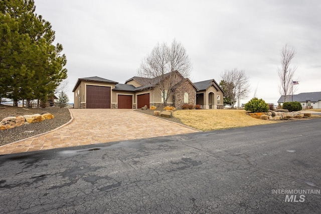 view of front of home featuring a garage, stone siding, driveway, and stucco siding