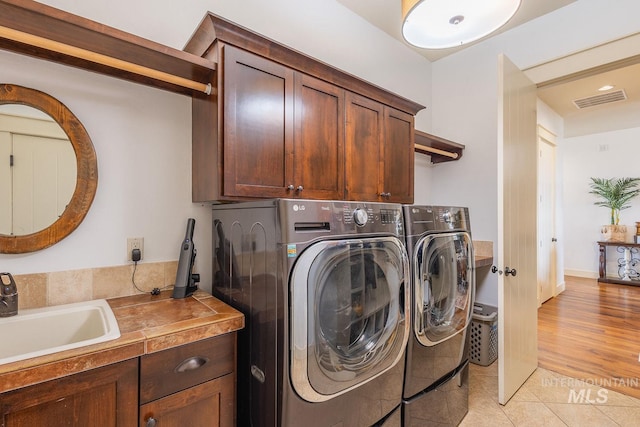 clothes washing area with washing machine and clothes dryer, cabinet space, visible vents, and a sink