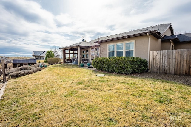 rear view of house with a patio area, stucco siding, a yard, and fence