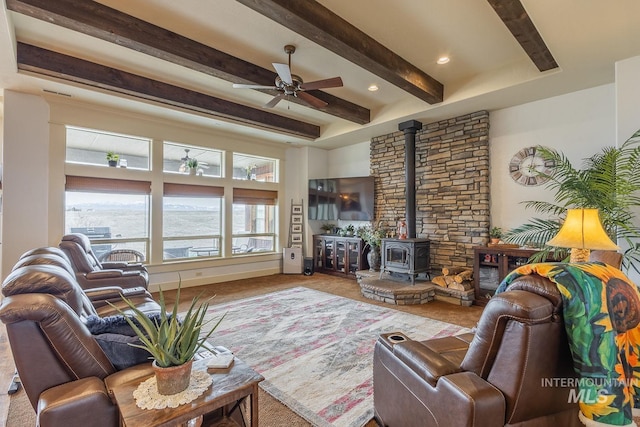 living room featuring a wood stove, a ceiling fan, beamed ceiling, and baseboards