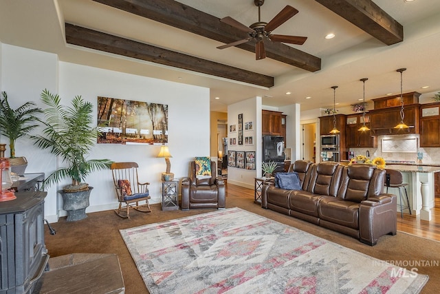 living room featuring beam ceiling, baseboards, a wood stove, and a ceiling fan