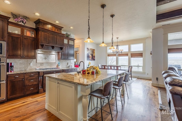 kitchen with light stone counters, light wood finished floors, a sink, a kitchen bar, and tasteful backsplash