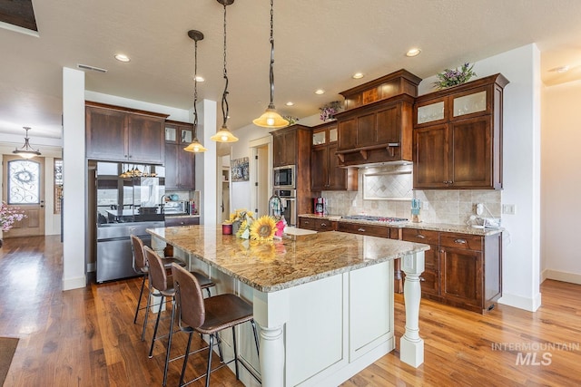 kitchen featuring light wood-type flooring, decorative backsplash, a kitchen breakfast bar, and appliances with stainless steel finishes