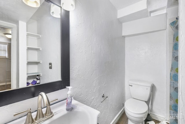 bathroom with toilet, baseboards, a sink, and a textured wall