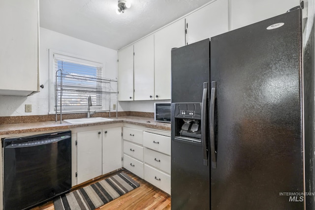 kitchen with black appliances, wood finished floors, a sink, and white cabinets