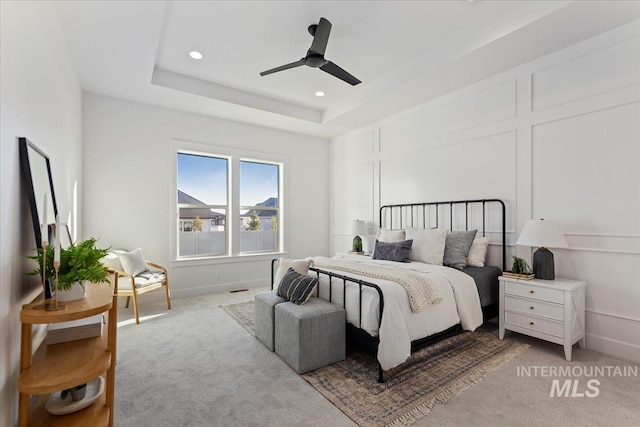 carpeted bedroom featuring a tray ceiling and ceiling fan