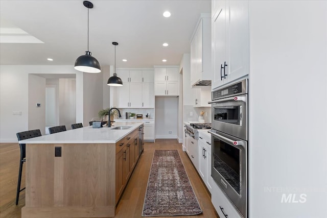 kitchen featuring sink, white cabinetry, hanging light fixtures, and an island with sink