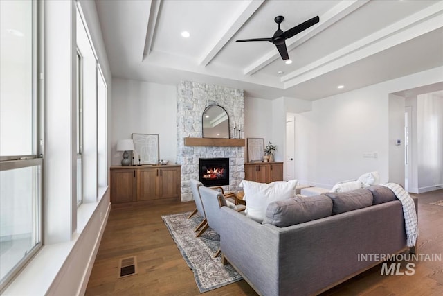 living room featuring ceiling fan, dark hardwood / wood-style floors, a stone fireplace, and a healthy amount of sunlight