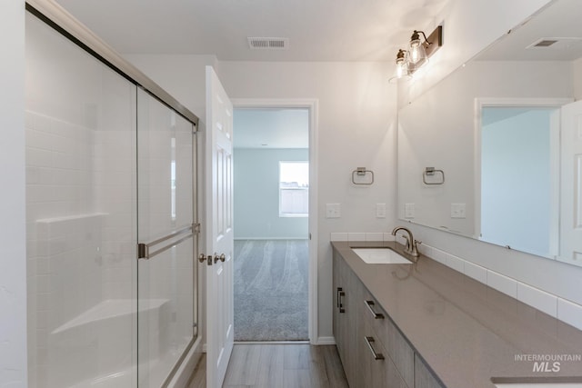 full bath featuring vanity, a shower stall, visible vents, and wood finished floors