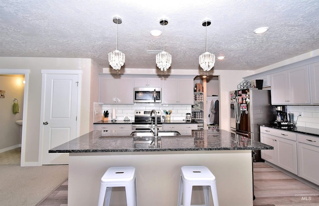 kitchen featuring a breakfast bar area, a center island with sink, tasteful backsplash, a sink, and appliances with stainless steel finishes