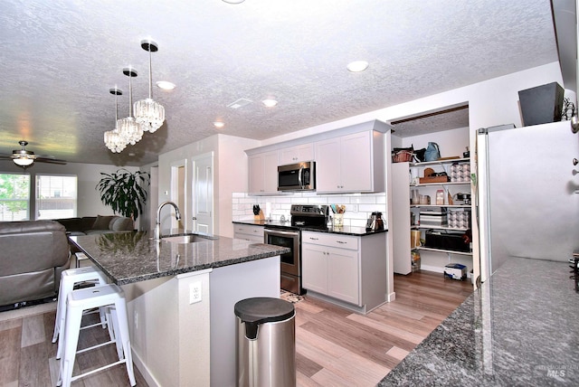 kitchen featuring stainless steel appliances, a textured ceiling, a sink, and light wood-type flooring