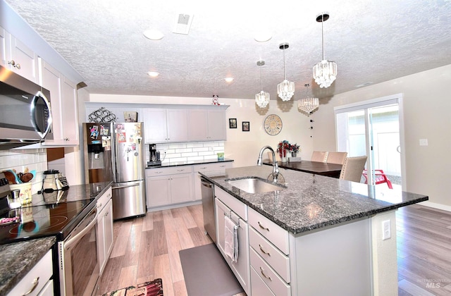 kitchen with appliances with stainless steel finishes, tasteful backsplash, a sink, a textured ceiling, and light wood-type flooring