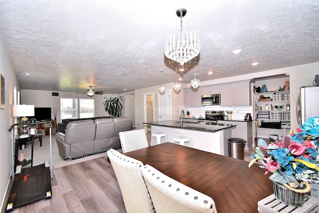 dining room featuring light wood-style floors, ceiling fan with notable chandelier, recessed lighting, and a textured ceiling