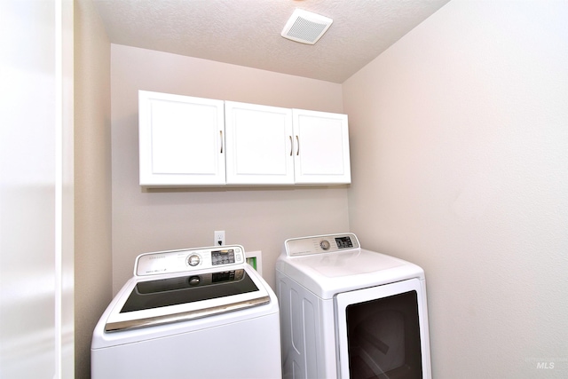 laundry area featuring a textured ceiling, washing machine and clothes dryer, cabinet space, and visible vents