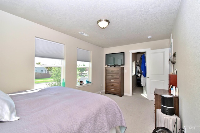 bedroom featuring visible vents, baseboards, a walk in closet, light colored carpet, and a textured ceiling
