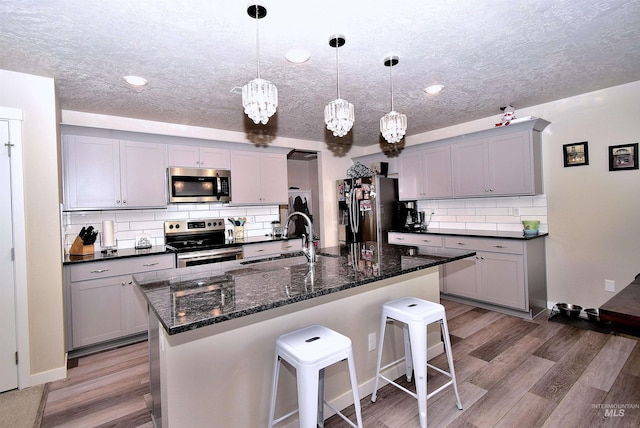 kitchen with a sink, a textured ceiling, appliances with stainless steel finishes, and a kitchen bar