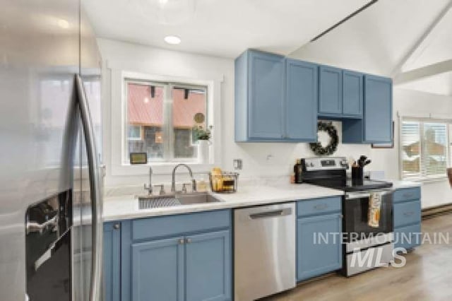 kitchen with blue cabinetry, stainless steel appliances, light hardwood / wood-style floors, and sink