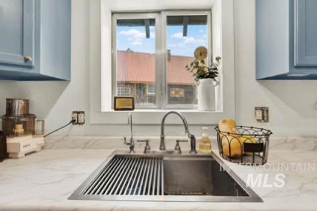 kitchen featuring light stone counters, blue cabinets, and sink