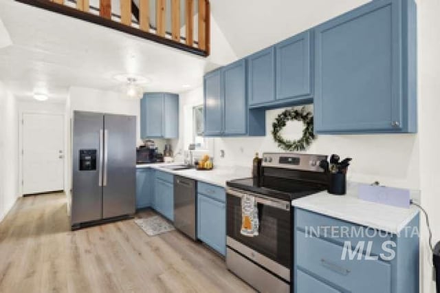 kitchen with stainless steel appliances, sink, blue cabinets, and light hardwood / wood-style flooring