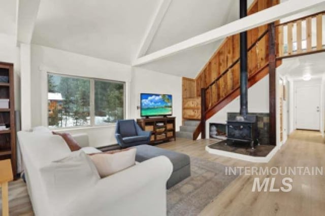 living room featuring high vaulted ceiling, light hardwood / wood-style floors, and a wood stove