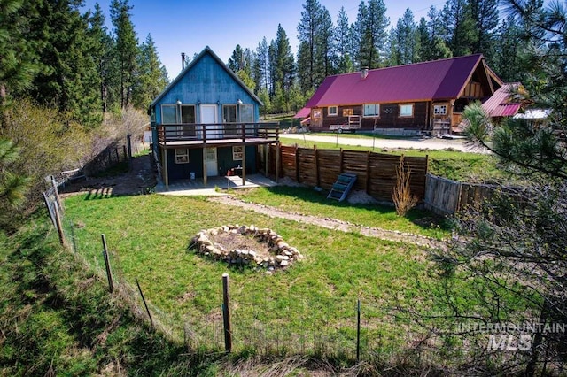 back of property with a fenced backyard, metal roof, a wooden deck, a lawn, and a patio