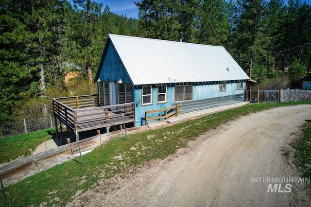 view of front of home with fence, a view of trees, dirt driveway, and metal roof