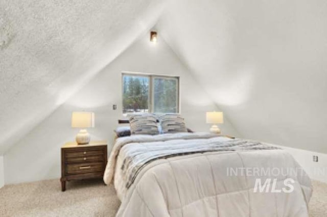 carpeted bedroom featuring vaulted ceiling and a textured ceiling