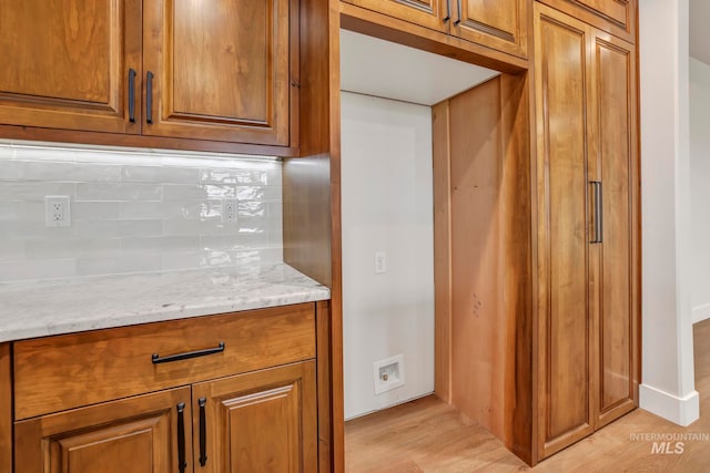 kitchen with light stone counters, light wood-type flooring, backsplash, and brown cabinets