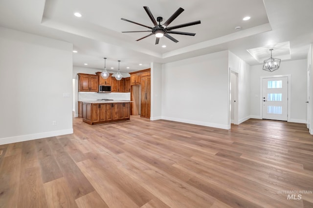 unfurnished living room featuring recessed lighting, baseboards, light wood-style flooring, a tray ceiling, and ceiling fan with notable chandelier