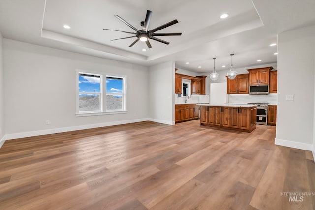 unfurnished living room featuring light wood-type flooring, a tray ceiling, and baseboards