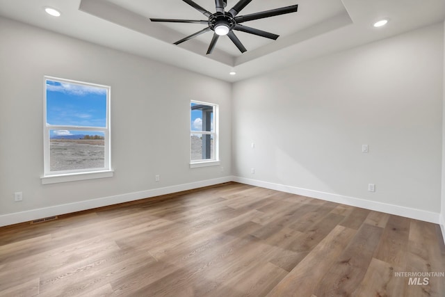 spare room featuring a tray ceiling, baseboards, and wood finished floors