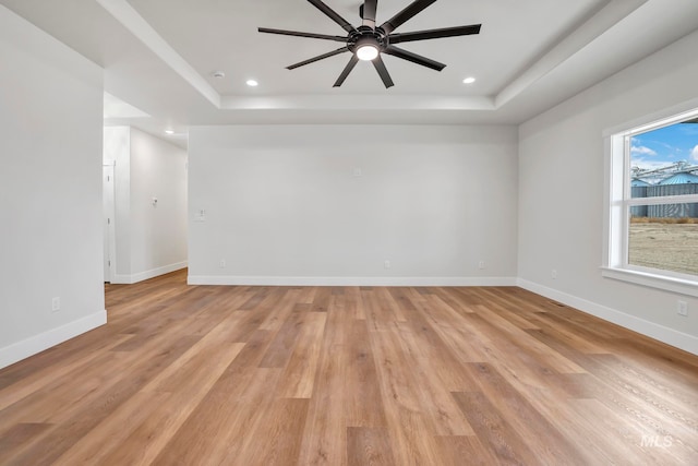 unfurnished room featuring baseboards, a tray ceiling, and light wood-style flooring