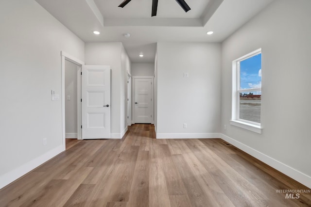 spare room featuring recessed lighting, a ceiling fan, baseboards, light wood-type flooring, and a raised ceiling