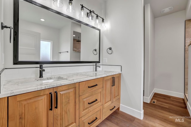 full bathroom featuring wood finished floors, tiled shower, a sink, and baseboards