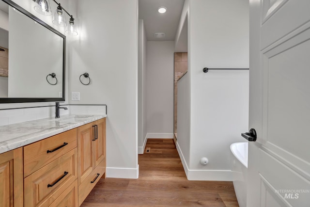 bathroom with wood finished floors, vanity, baseboards, a tub, and walk in shower