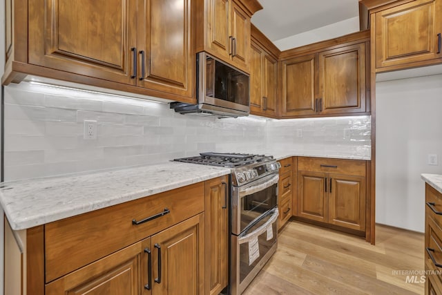 kitchen with tasteful backsplash, stainless steel appliances, light wood finished floors, and brown cabinets