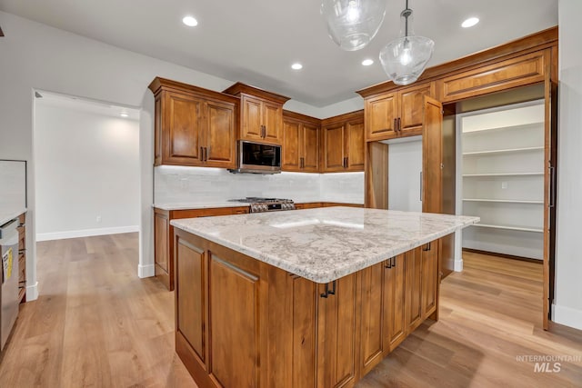 kitchen with light wood-style flooring, decorative backsplash, brown cabinetry, light stone countertops, and stainless steel microwave