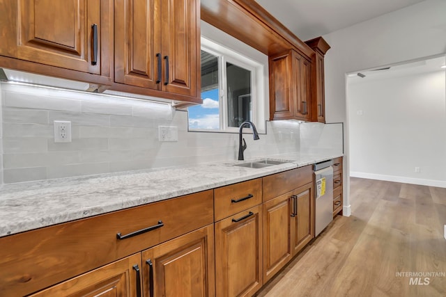 kitchen with a sink, stainless steel dishwasher, light wood-type flooring, brown cabinets, and light stone countertops