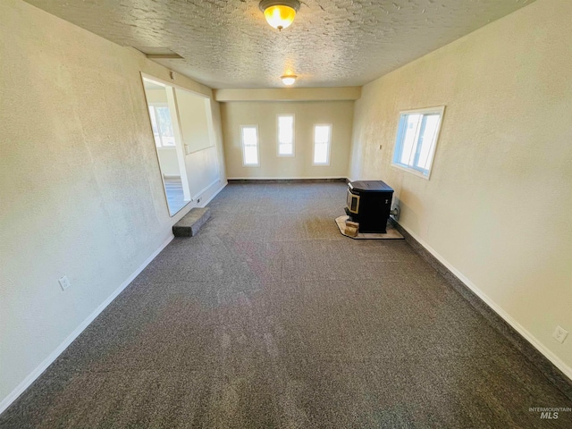 carpeted spare room with a wood stove and a textured ceiling