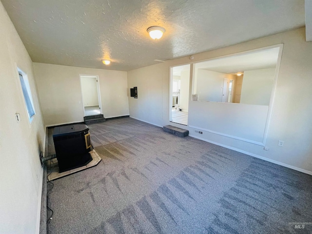 unfurnished living room featuring a textured ceiling, carpet flooring, heating unit, and a wood stove