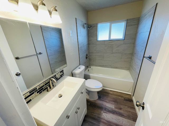 full bathroom with wood-type flooring, a textured ceiling, vanity, tiled shower / bath, and toilet