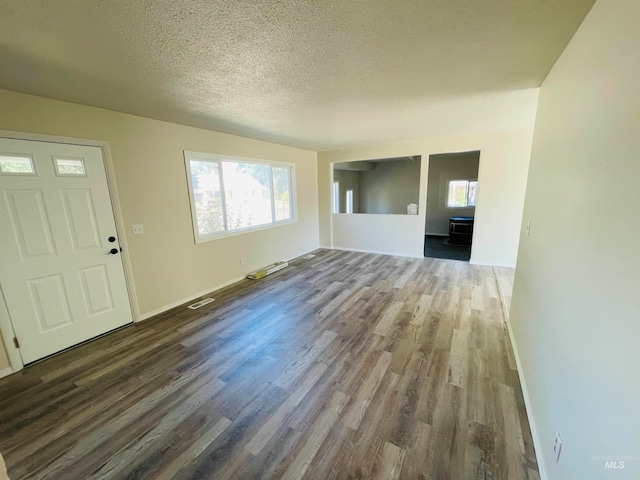 unfurnished living room with a wealth of natural light, a textured ceiling, and dark hardwood / wood-style flooring