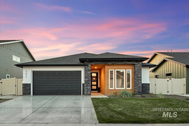 prairie-style house featuring stone siding, an attached garage, a gate, and concrete driveway