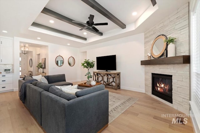 living room with a tray ceiling, light wood finished floors, a fireplace, beam ceiling, and recessed lighting