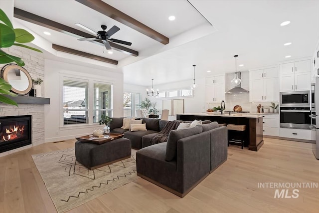 living room with ceiling fan with notable chandelier, light wood-style flooring, a stone fireplace, and recessed lighting