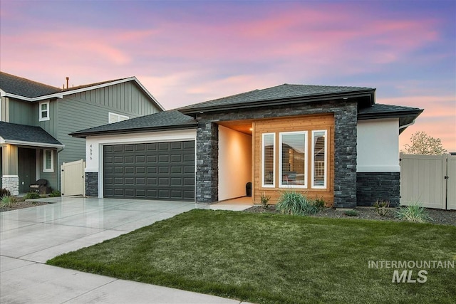 prairie-style house featuring fence, concrete driveway, stone siding, a lawn, and a garage